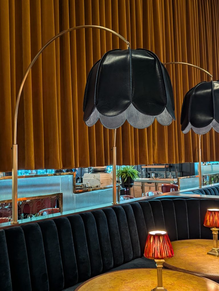 Bespoke dark blue leather pendants with scalloped edges on antique brass arc bases over restaurant banquettes
